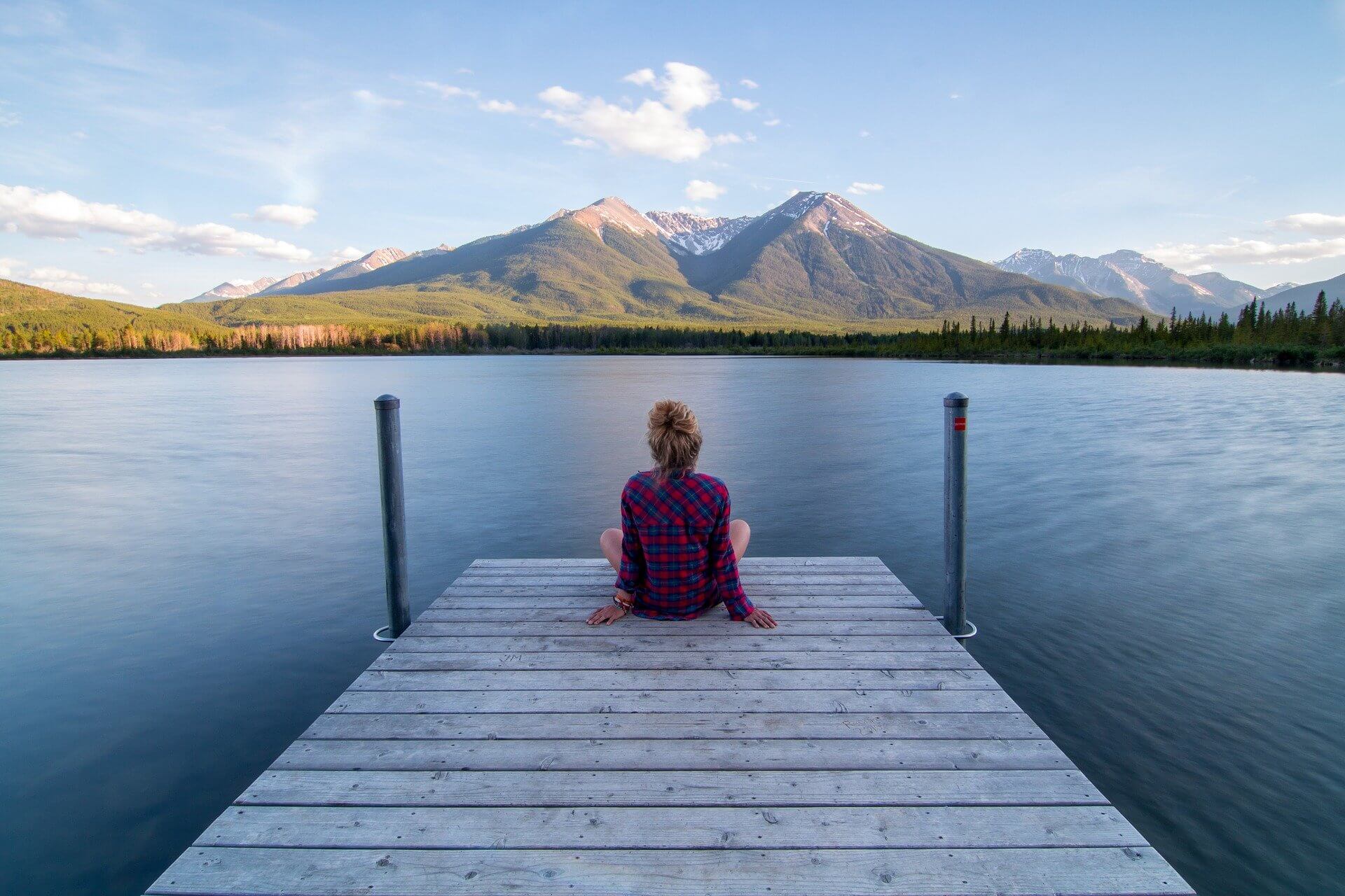 Femme assise en tailleur sur un ponton face aux montagnes